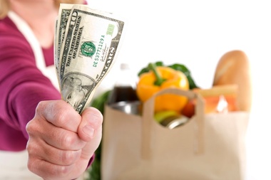 Woman holding out money in front of groceries