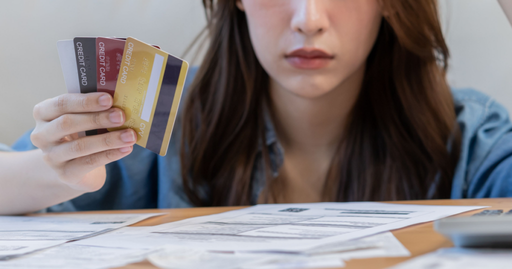 A woman holding credit cards contemplating How Can I Manage Debt When I Don’t Know Where to Start?