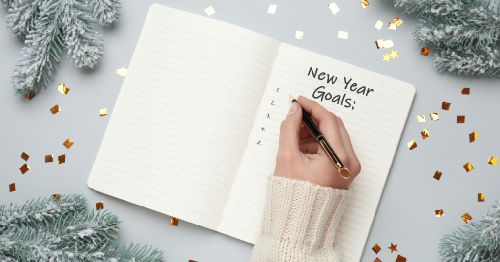 A person writing New Year Resolutions in a notebook on a festive table
