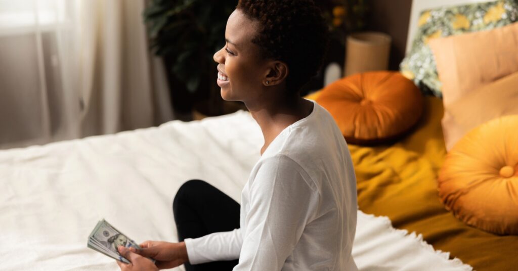 woman sitting on bed looking relieved with cash on her hand