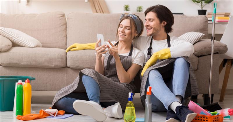 a couple checking their phone seated on the floor with cleaning supplies around them